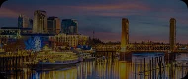 Sacramento waterfront skyline with a bridge and ferris wheel reflected at sunset