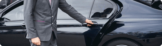 A chauffeur in a formal suit opens the luxury car door, offering a smooth cruise port pickup experience.