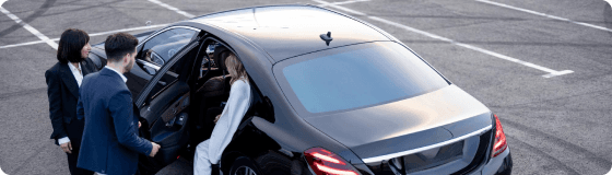 Hotel guests greeted by a chauffeur beside a sleek sedan, ensuring premium hospitality transportation.