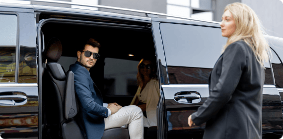 A man is seated in a luxury van with the door open as a woman approaches, ready for a premium group ride.
