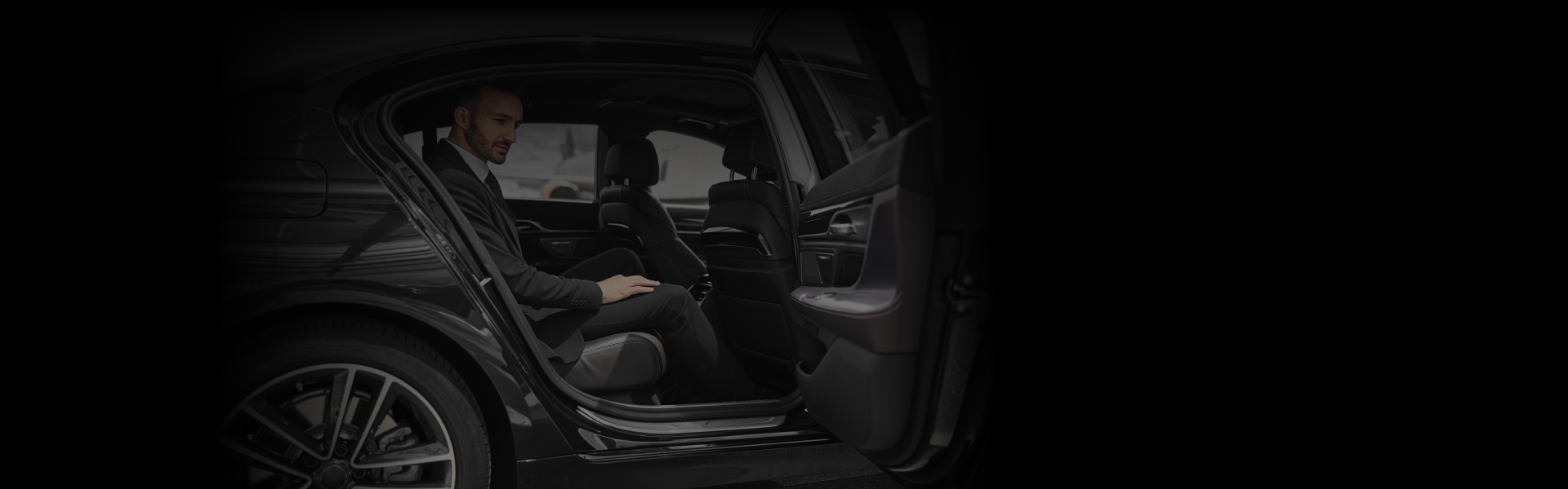 Corporate Event Transportation featuring a sharply dressed man seated in a sleek black luxury sedan, viewed from a wide open-door angle.